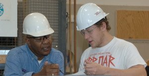 Two men in hard hats -- the older one instructing the younger.